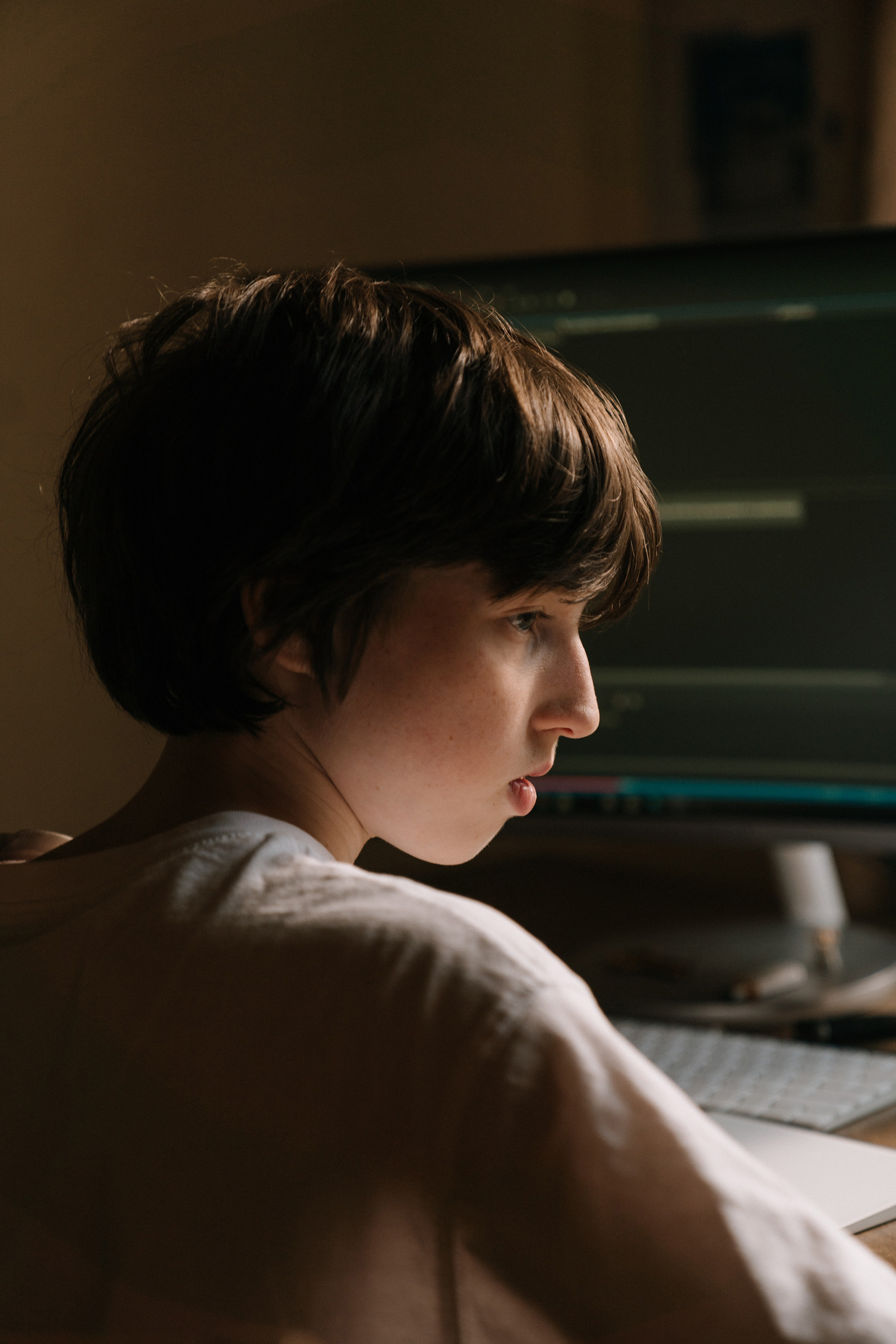 A person is facing a computer screen in a dimly lit room, seemingly engaged in work or study.